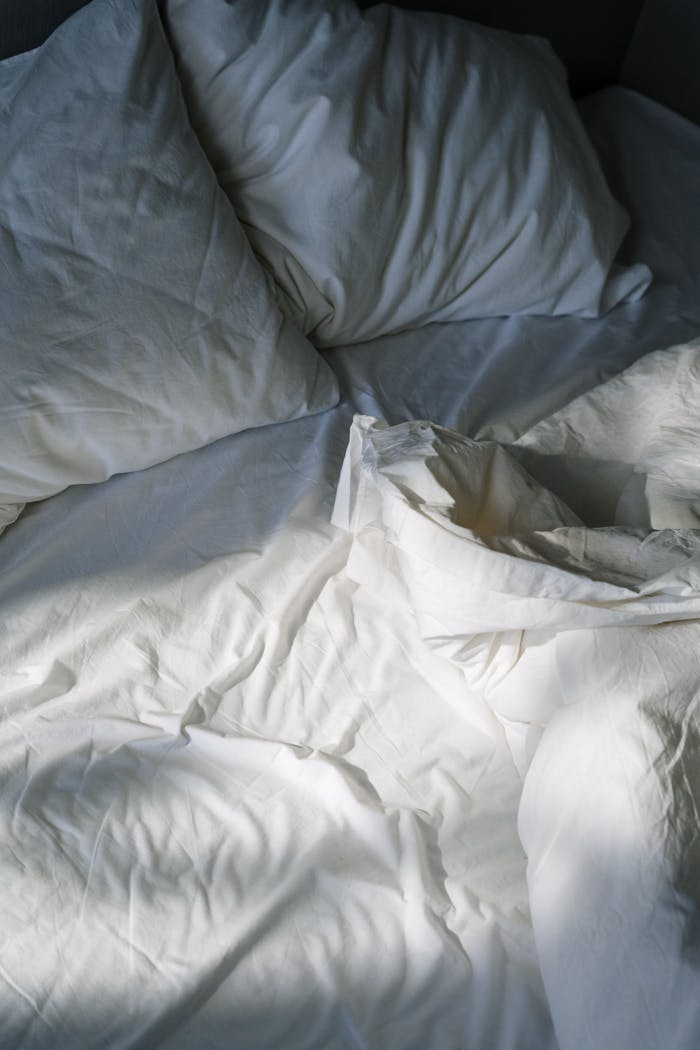 A cozy, inviting bed with white linens lit by morning sunlight, creating a restful atmosphere.